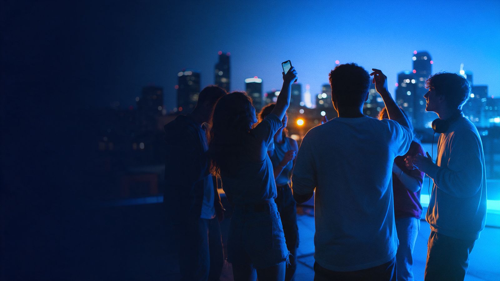 Friends on a city rooftop at night sharing a new track, one holding a phone up