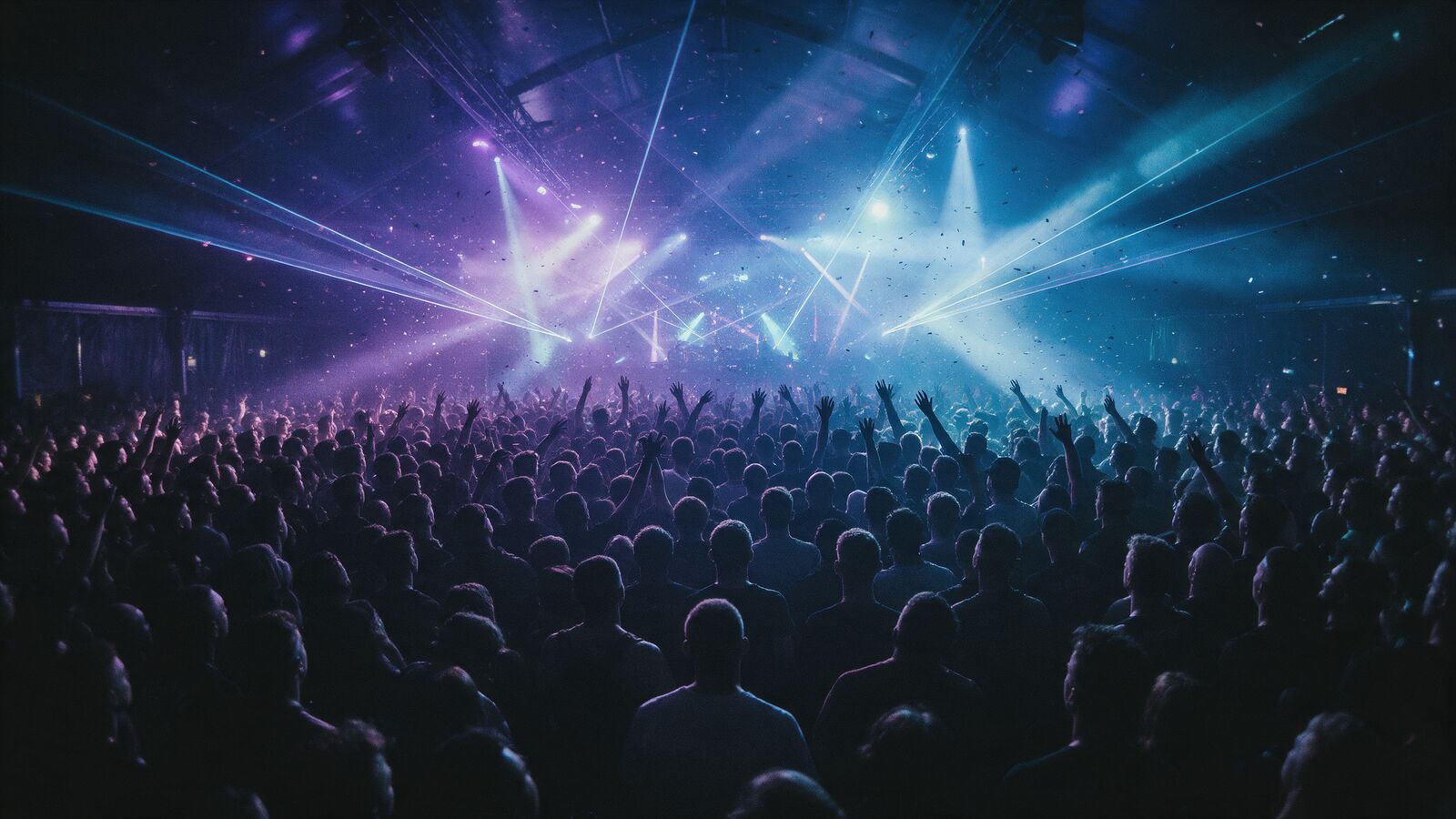 A packed crowd with hands raised under purple and blue stage lights